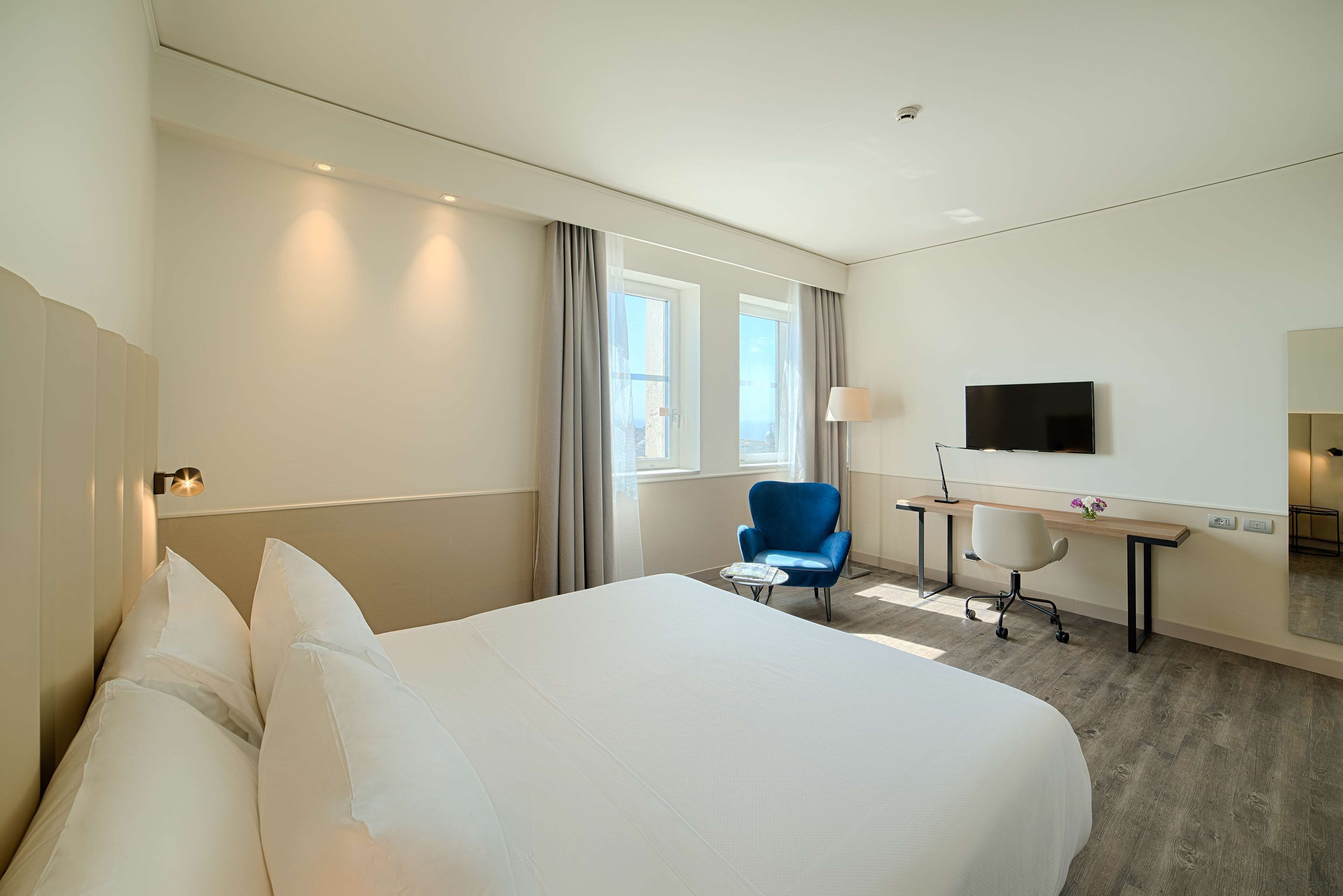 A hotel room with a large bed, a desk, a chair, a TV, and a window with curtains.