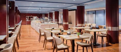 A spacious restaurant with wooden flooring, white chairs, and a central counter with a coffee station.