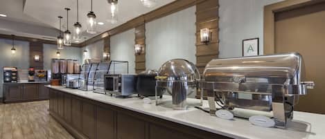 Buffet montado com diversos pontos de comida, incluindo uma churrasqueira, micro-ondas e máquina de café.