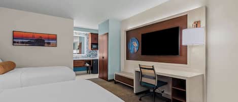 Una habitación de hotel con cama, escritorio, televisión y un cuadro.