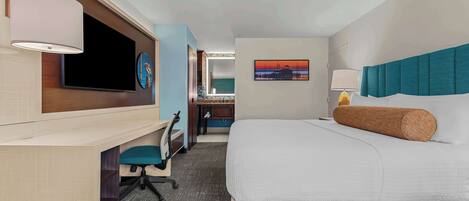 A hotel room with a bed, desk, chair, TV, artwork, and a lamp.