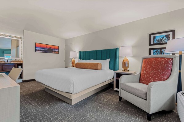A hotel room with a large bed, two bedside tables with lamps, a chair, a desk, and a mirror.