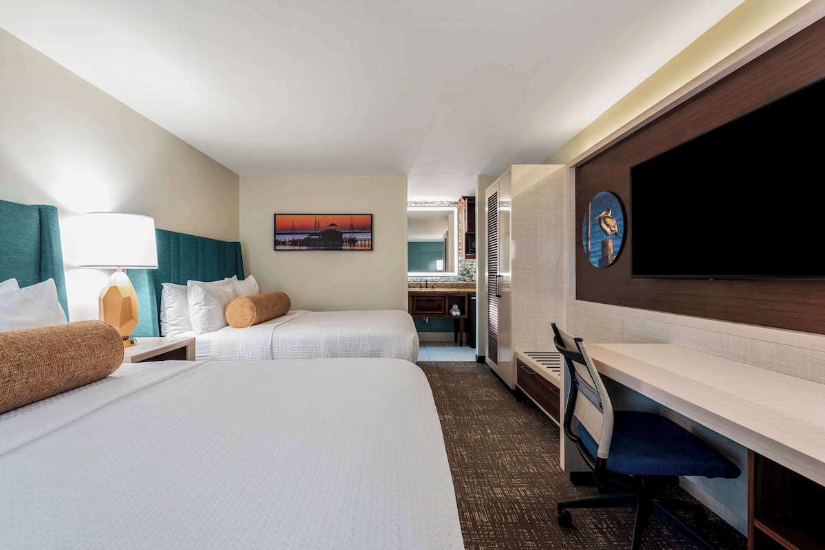 A hotel room with two beds, a desk, a TV, and a painting on the wall.