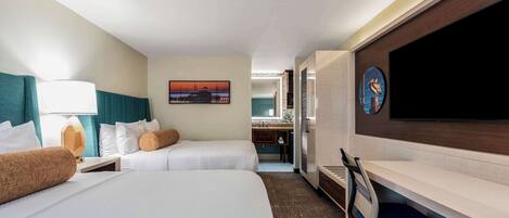 A hotel room with two beds, a desk, a TV, and a painting on the wall.