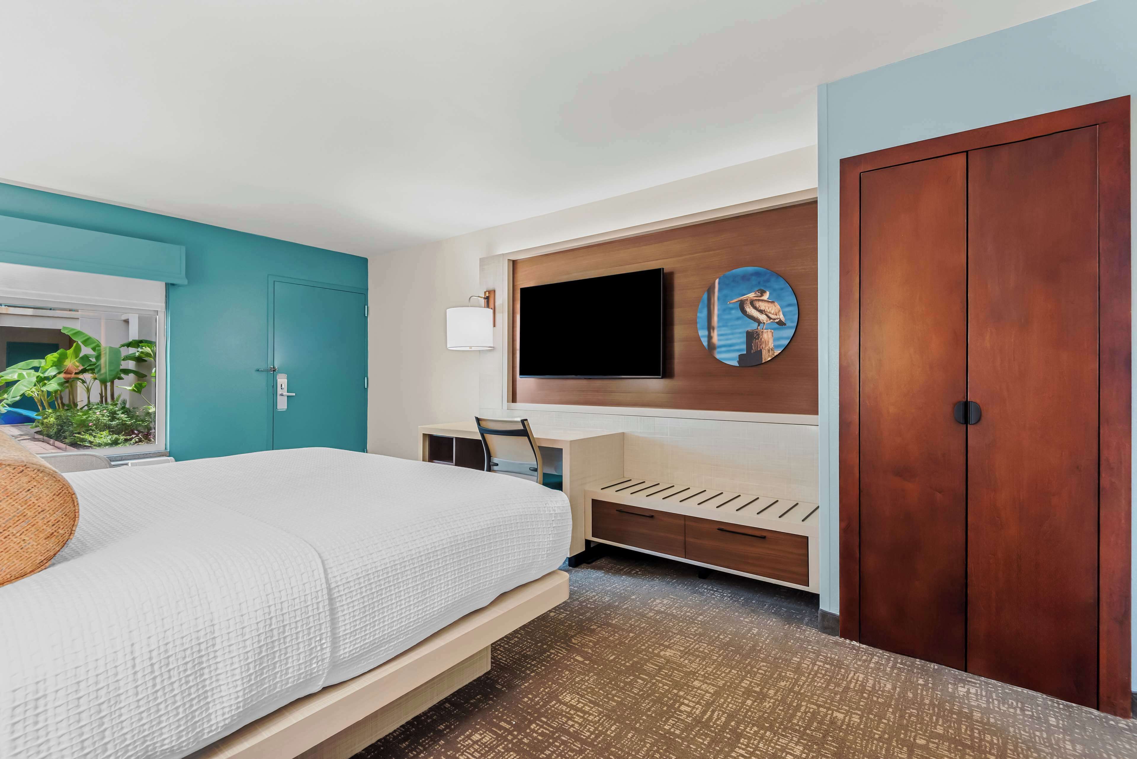 Ein Hotelzimmer mit einem Bett, einem Schreibtisch, einem an der Wand befestigten Fernseher und einem Kleiderschrank.