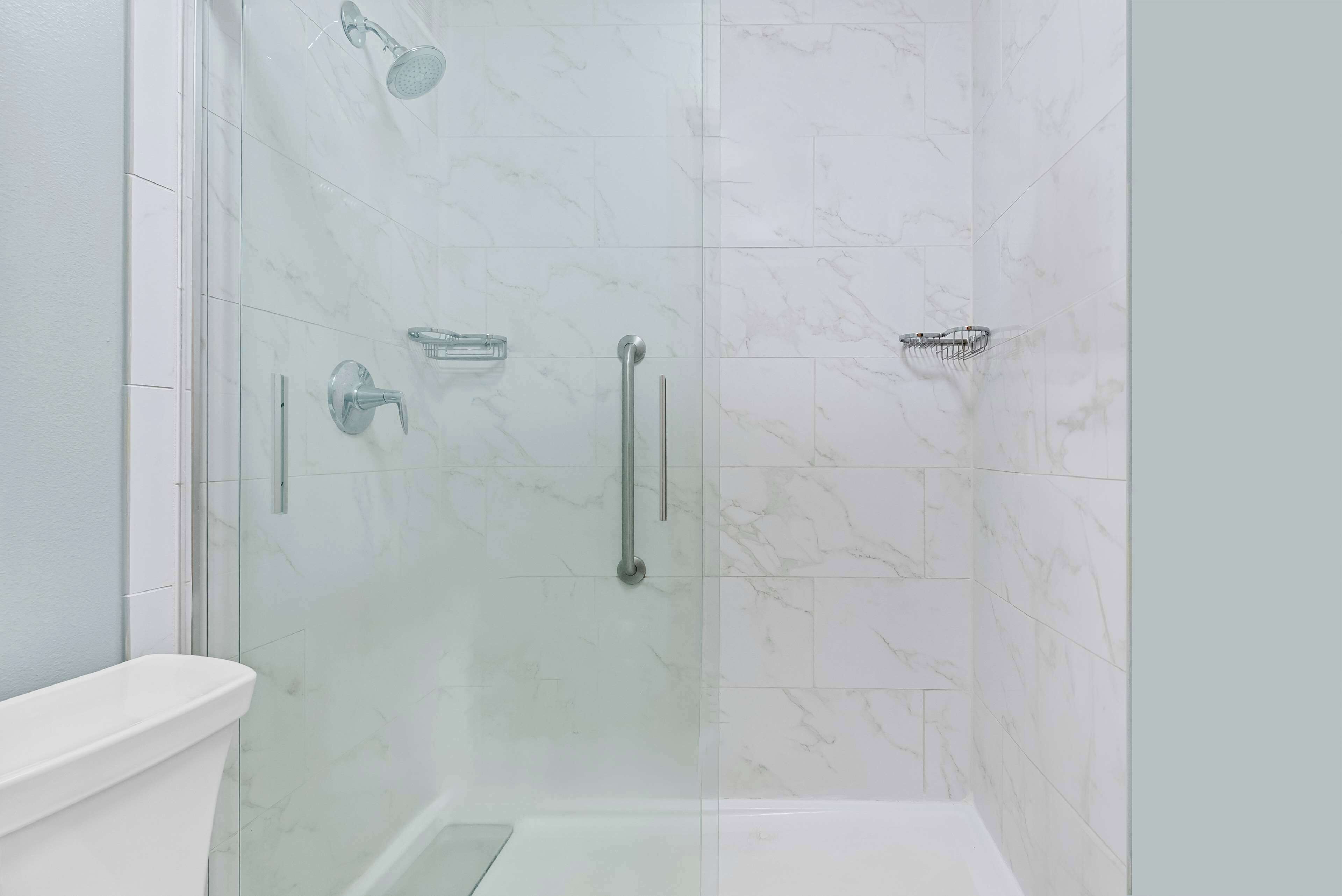 A glass-enclosed shower stall with a white toilet and marble tiles.