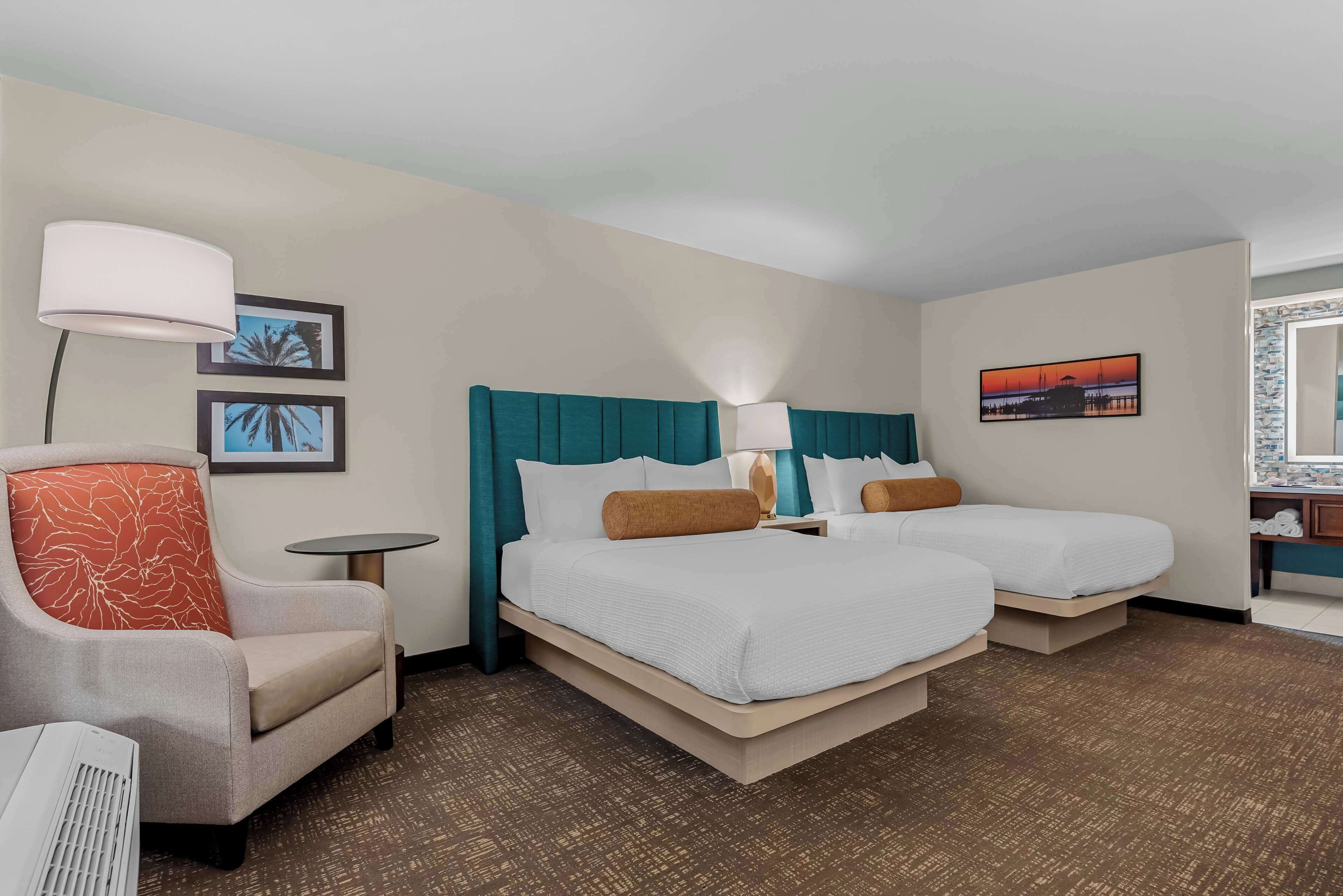 A hotel room with two beds, a chair, a small table, and a lamp.