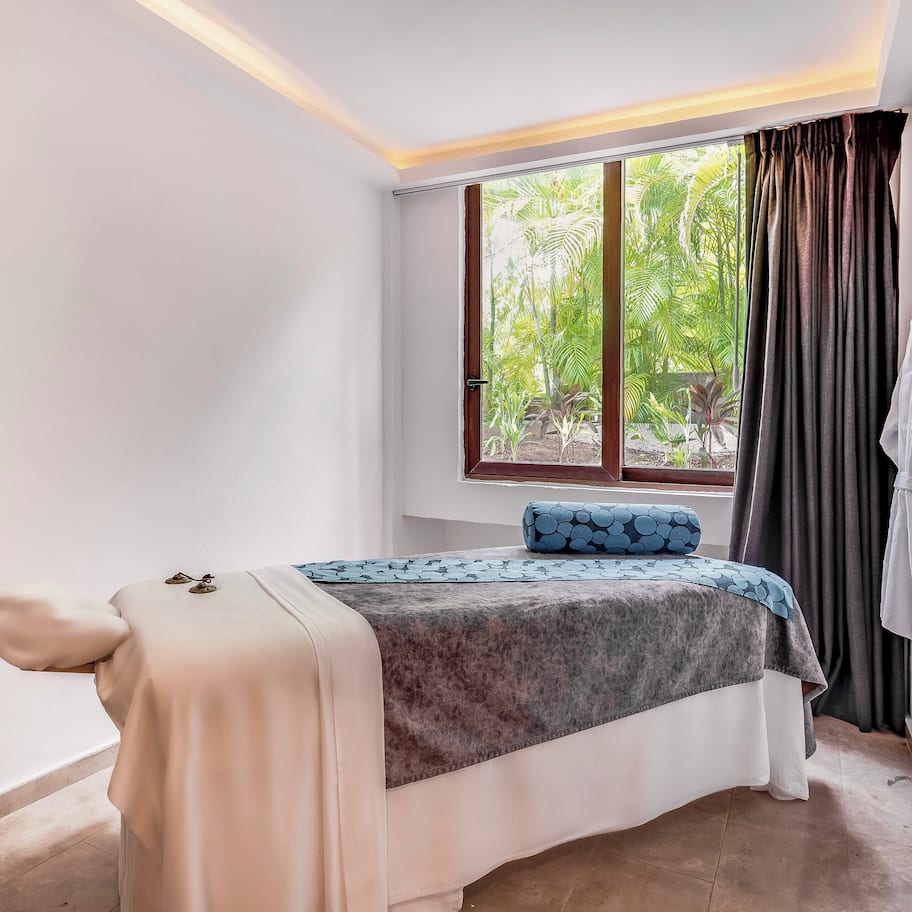 A single bed with a blue and grey patterned bedspread, a white pillow, and a white robe hanging on a hook.