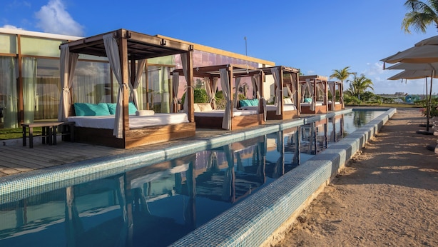 A poolside area with wooden cabanas and lounge chairs.