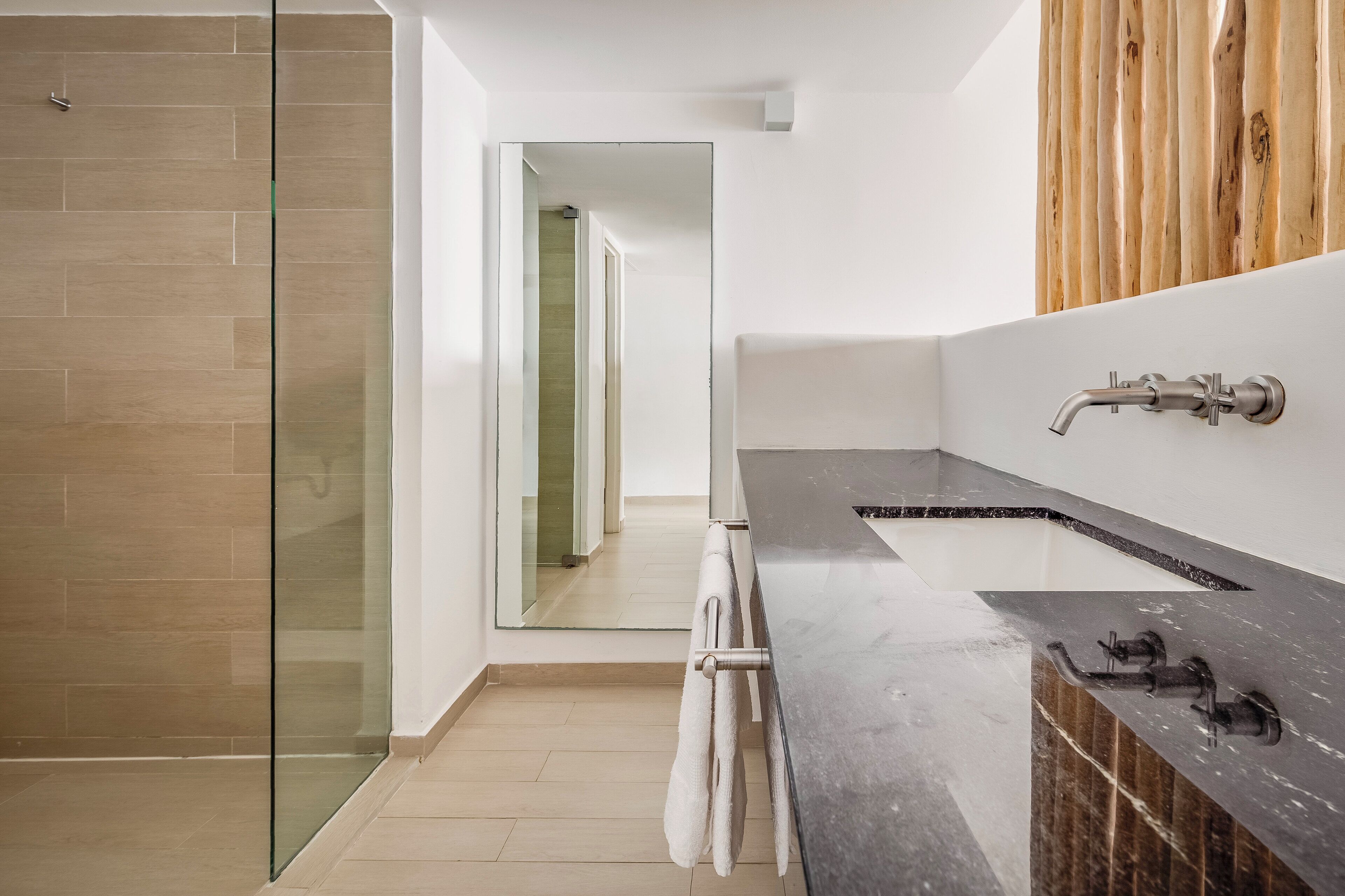 A modern bathroom with a glass shower enclosure, a dark marble countertop, and a wooden panel wall.