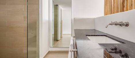 A modern bathroom with a glass shower enclosure, a dark marble countertop, and a wooden panel wall.