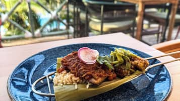 Un plato de comida con un borde azul, una mesa de madera y, al fondo, palmeras y una piscina.