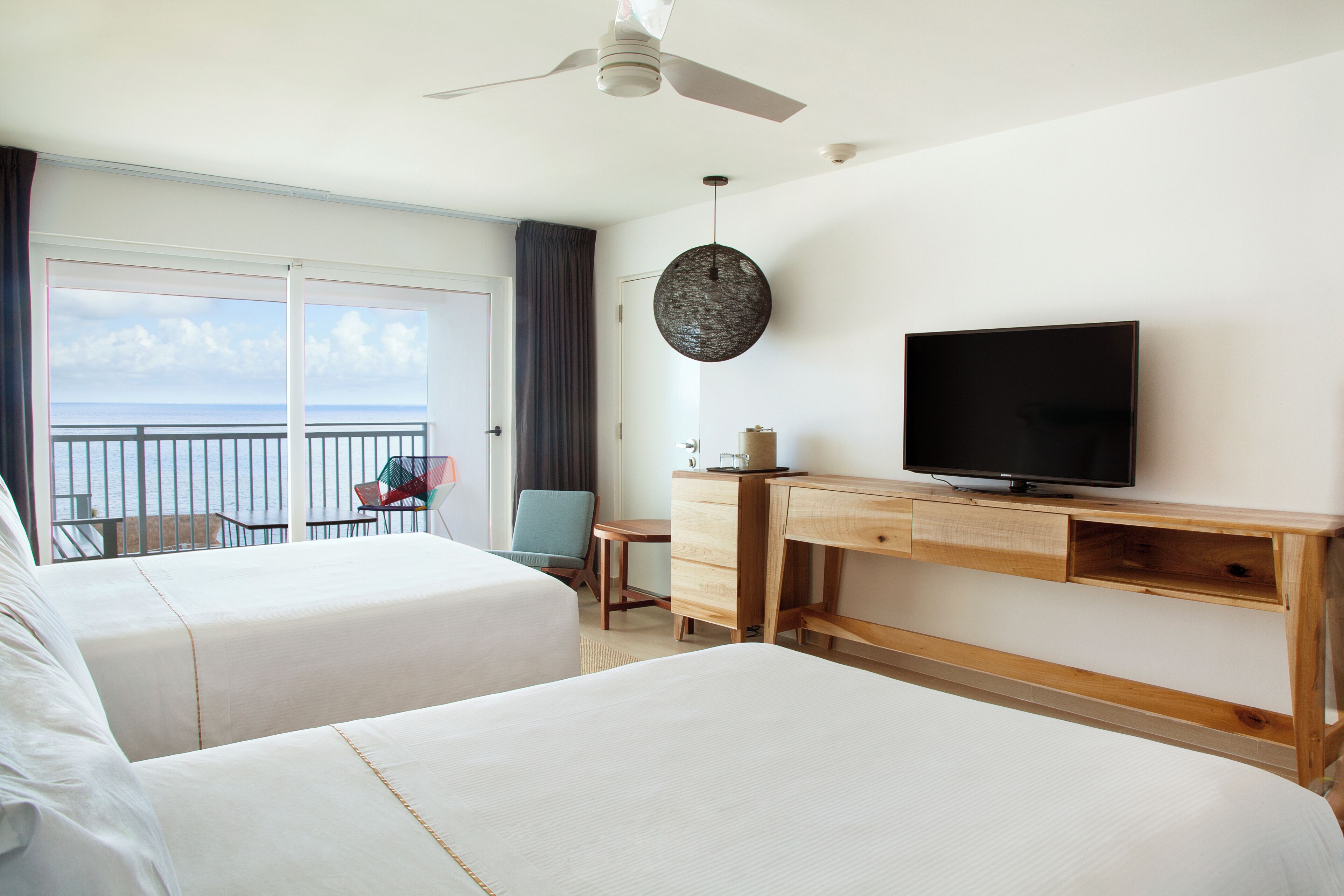 A hotel room with two beds, a TV, a desk, and a view of the ocean.