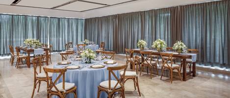 Un salón de banquetes con mesas redondas, sillas y centros de mesa florales.