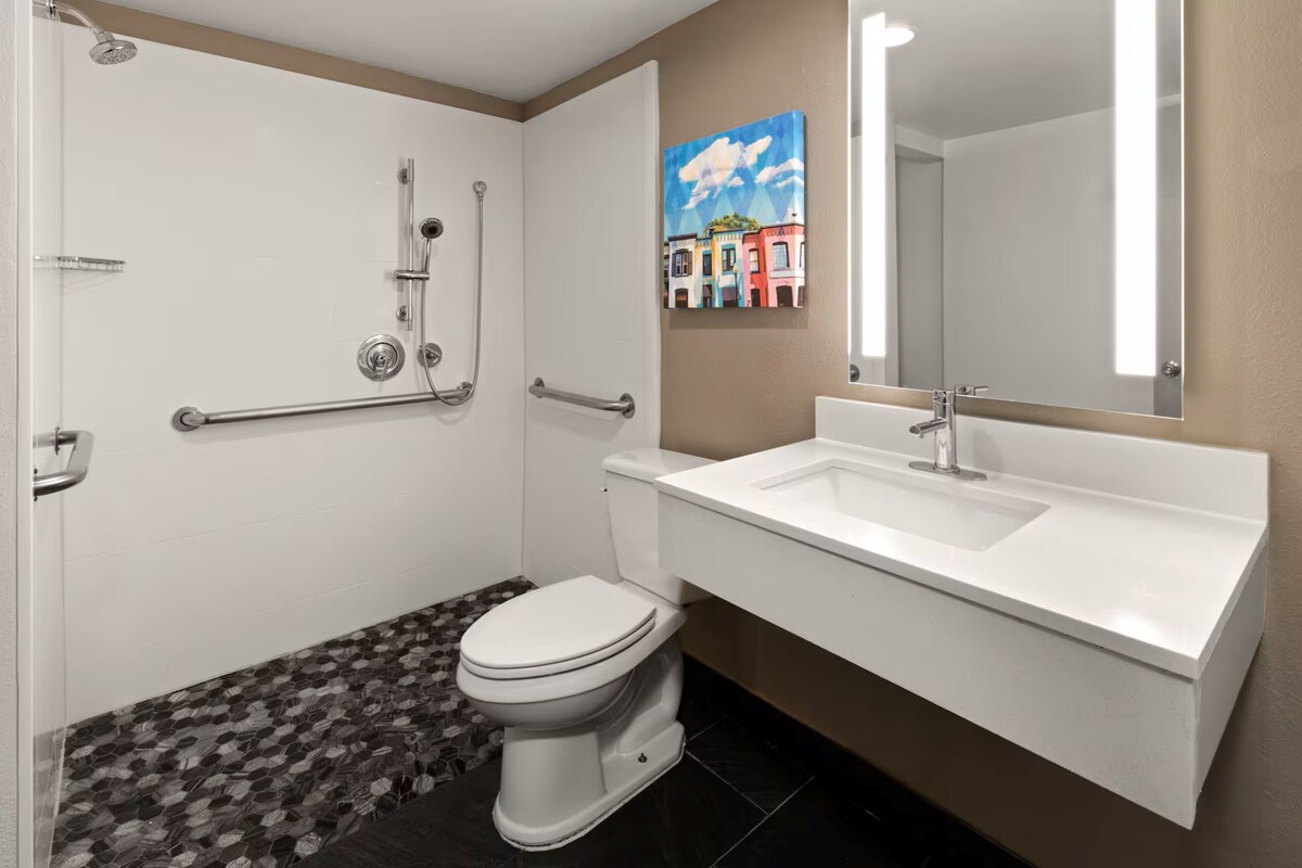 A bathroom with a shower, toilet, sink, and a mirror.