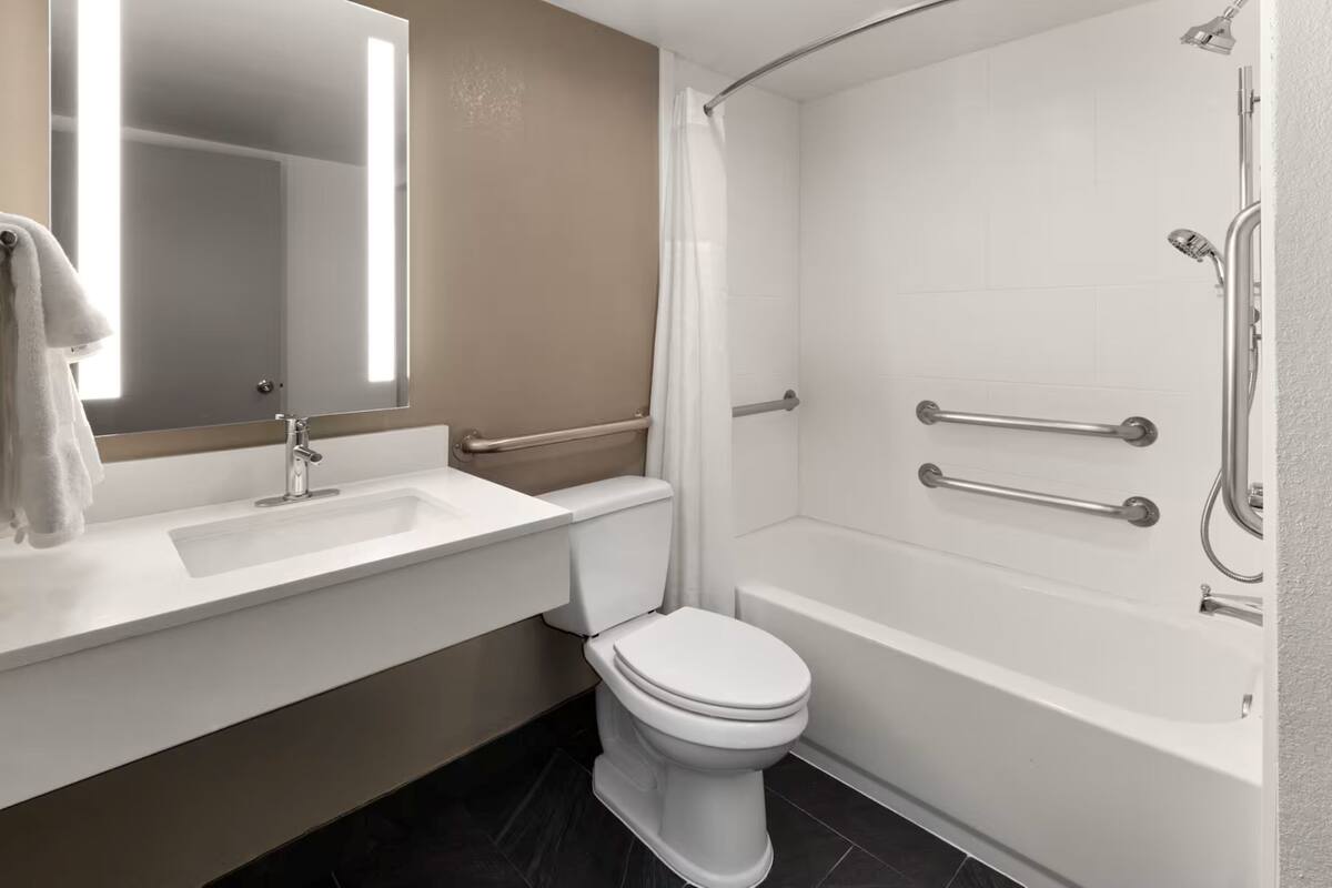 A bathroom with a white sink, toilet, and bathtub, equipped with grab bars and a shower curtain.