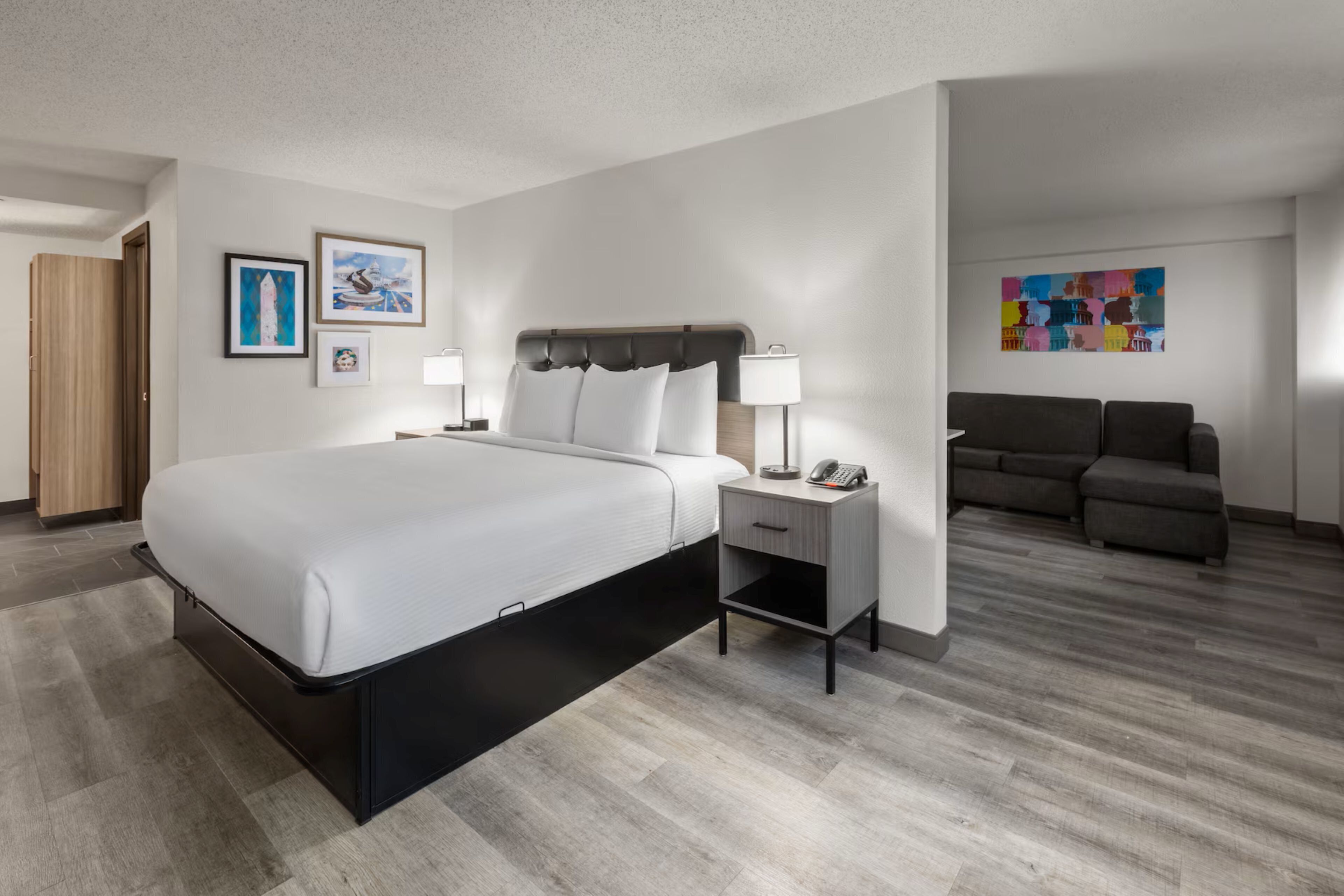 Una habitación de hotel con cama, mesita de noche, lámpara y un sofá.