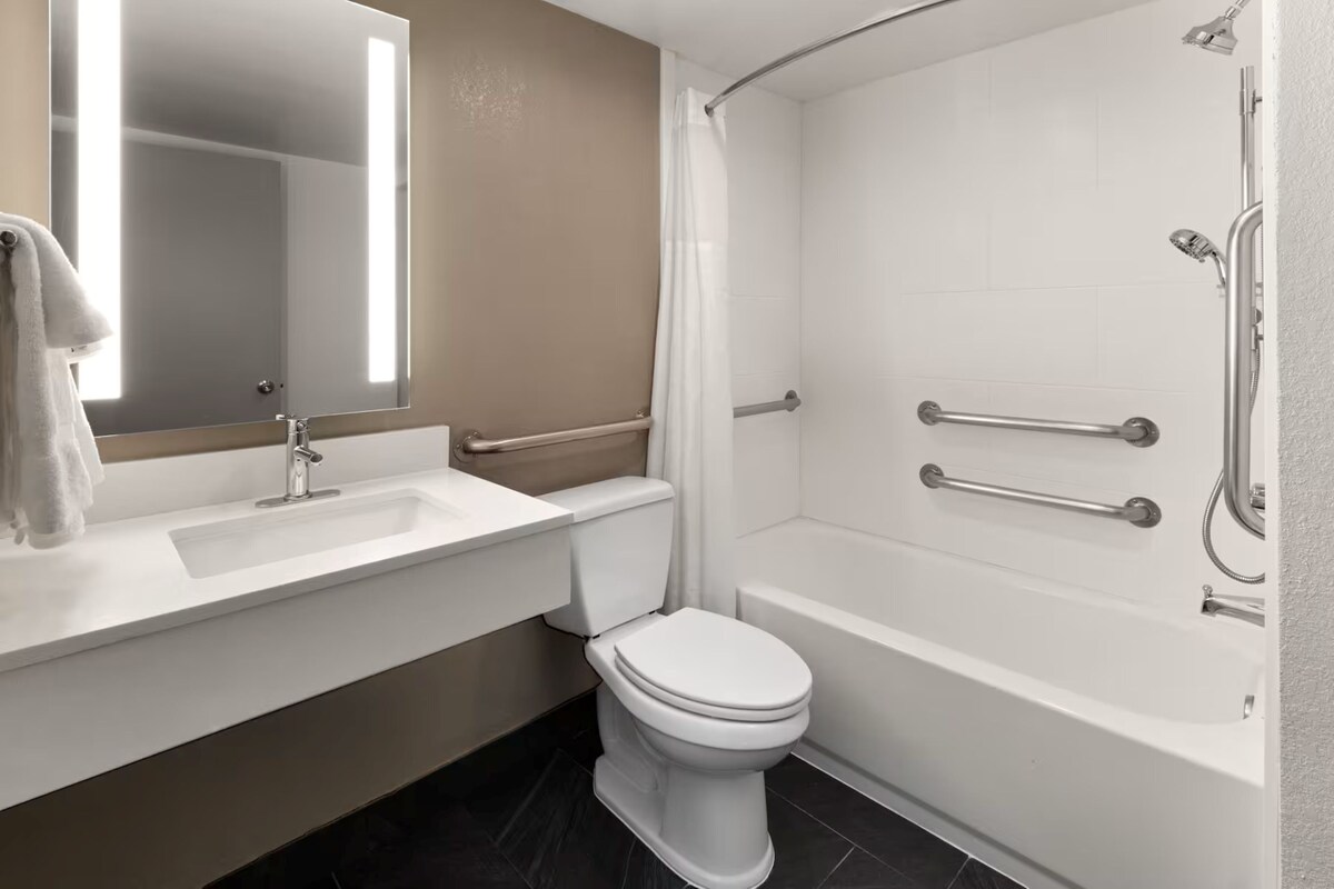 A bathroom with a white sink, toilet, and bathtub, equipped with grab bars and a shower curtain.