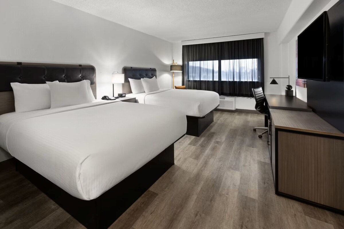A hotel room with two beds, a desk, a chair, a TV, and a window with curtains.