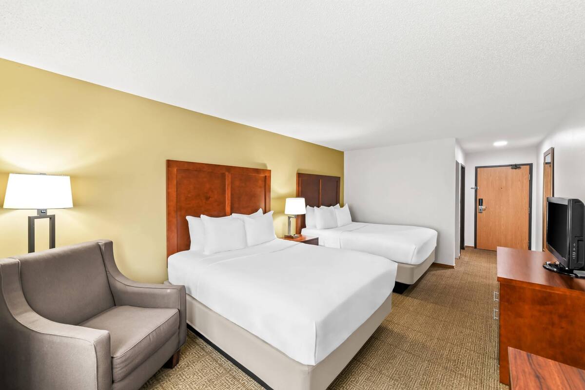 A hotel room with two beds, a sofa, a TV, and a desk.