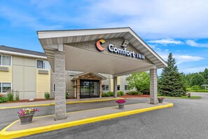 A Comfort Inn hotel entrance with a covered walkway, outdoor seating area, and a clear sky.
