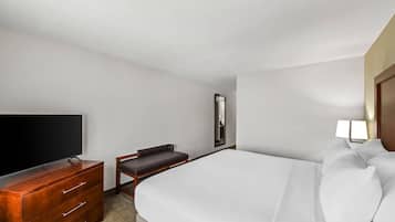 Une chambre d’hôtel avec un lit, un téléviseur posé sur une commode en bois, une chaise, une table de chevet et une lampe.