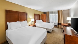 A hotel room with two beds, wooden headboards, a desk, a TV, and a window with curtains.