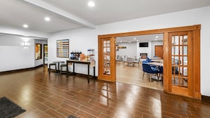 A spacious room with a wooden floor, a dining area with blue chairs, and a kitchen area with a stove and chairs.