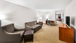 A hotel room with a sofa, a desk, a television, and a lamp.