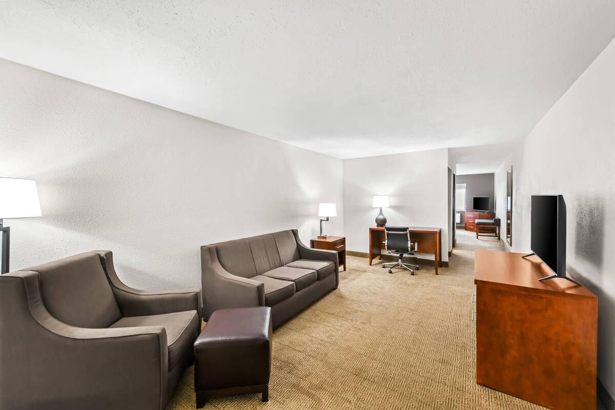 A hotel room with a sofa, a desk, a television, and a lamp.