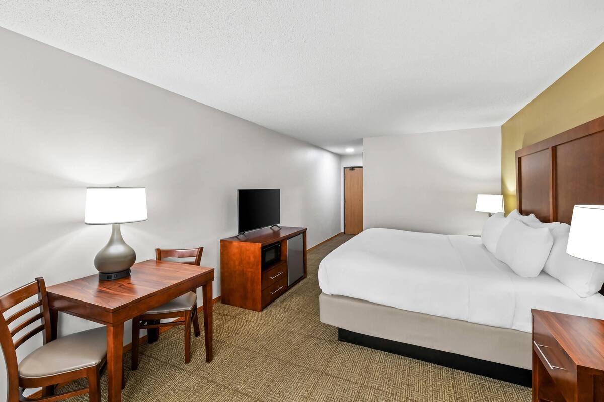 A hotel room with a bed, a desk with a lamp, a television, and a dresser.