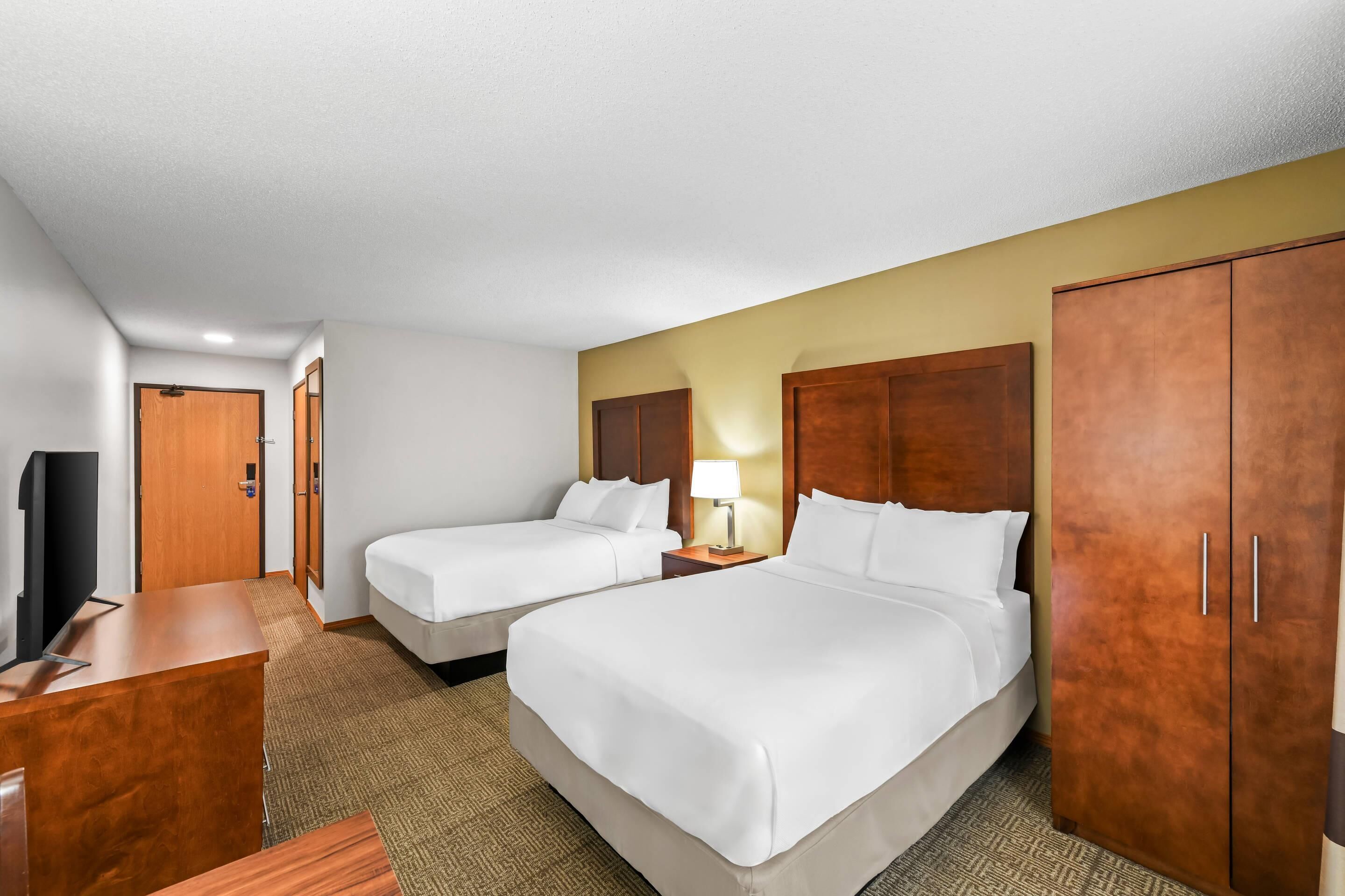 A hotel room with two beds, a desk, a TV, and a wardrobe.