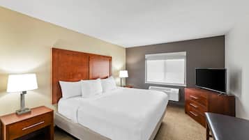 Habitación de hotel con una cama grande, cabecera de madera, dos mesitas de noche con lámparas, un televisor de pantalla plana y una ventana con persianas.