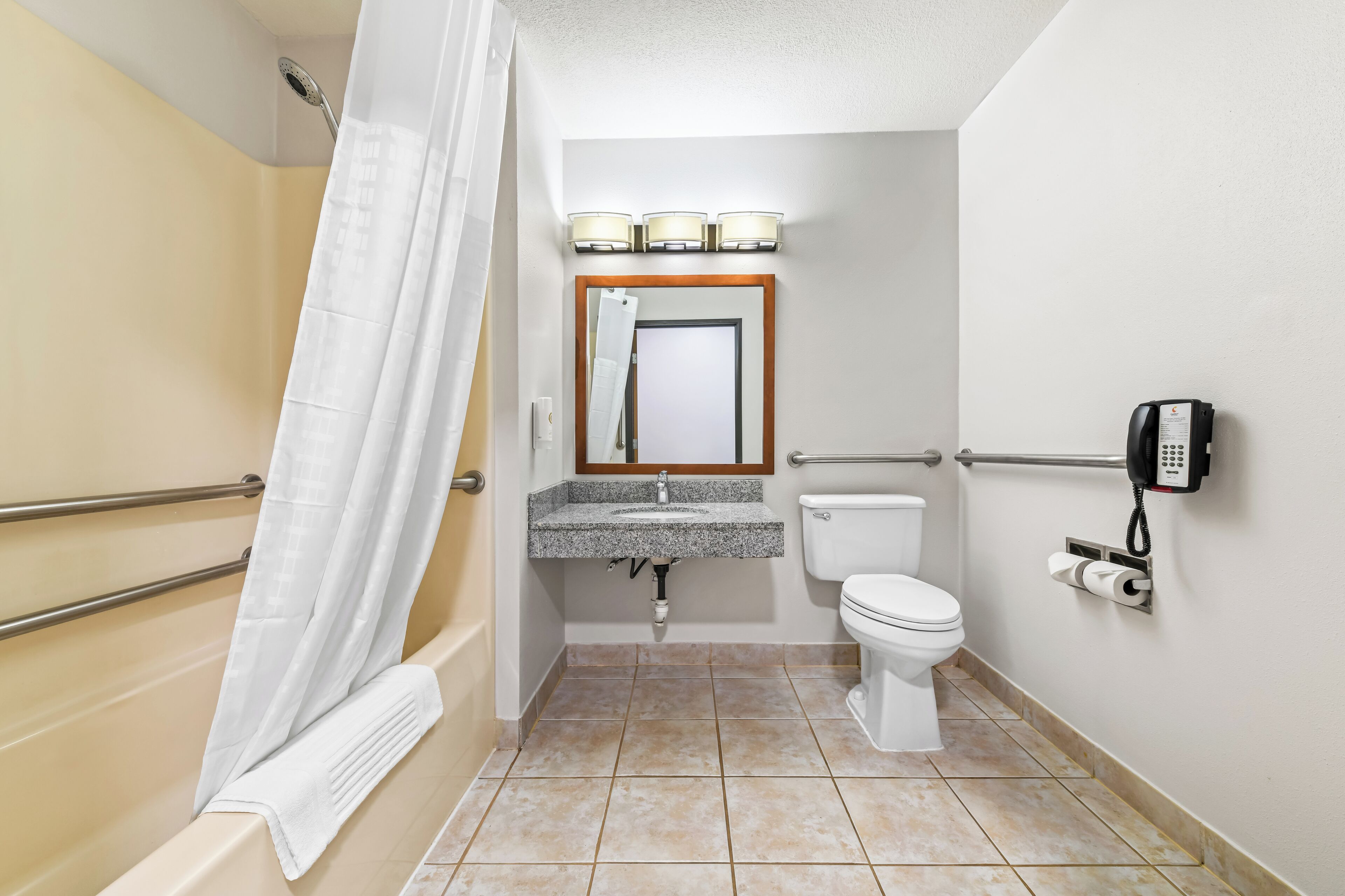 Un baño con ducha, inodoro, lavabo y un teléfono montado en la pared.