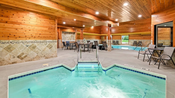 An indoor swimming pool with wooden walls and ceiling, surrounded by tables and chairs.