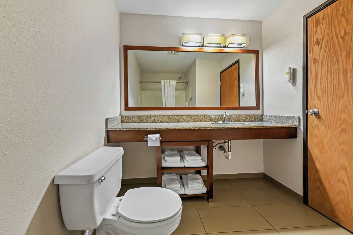 A bathroom with a toilet, sink, mirror, and towel rack.