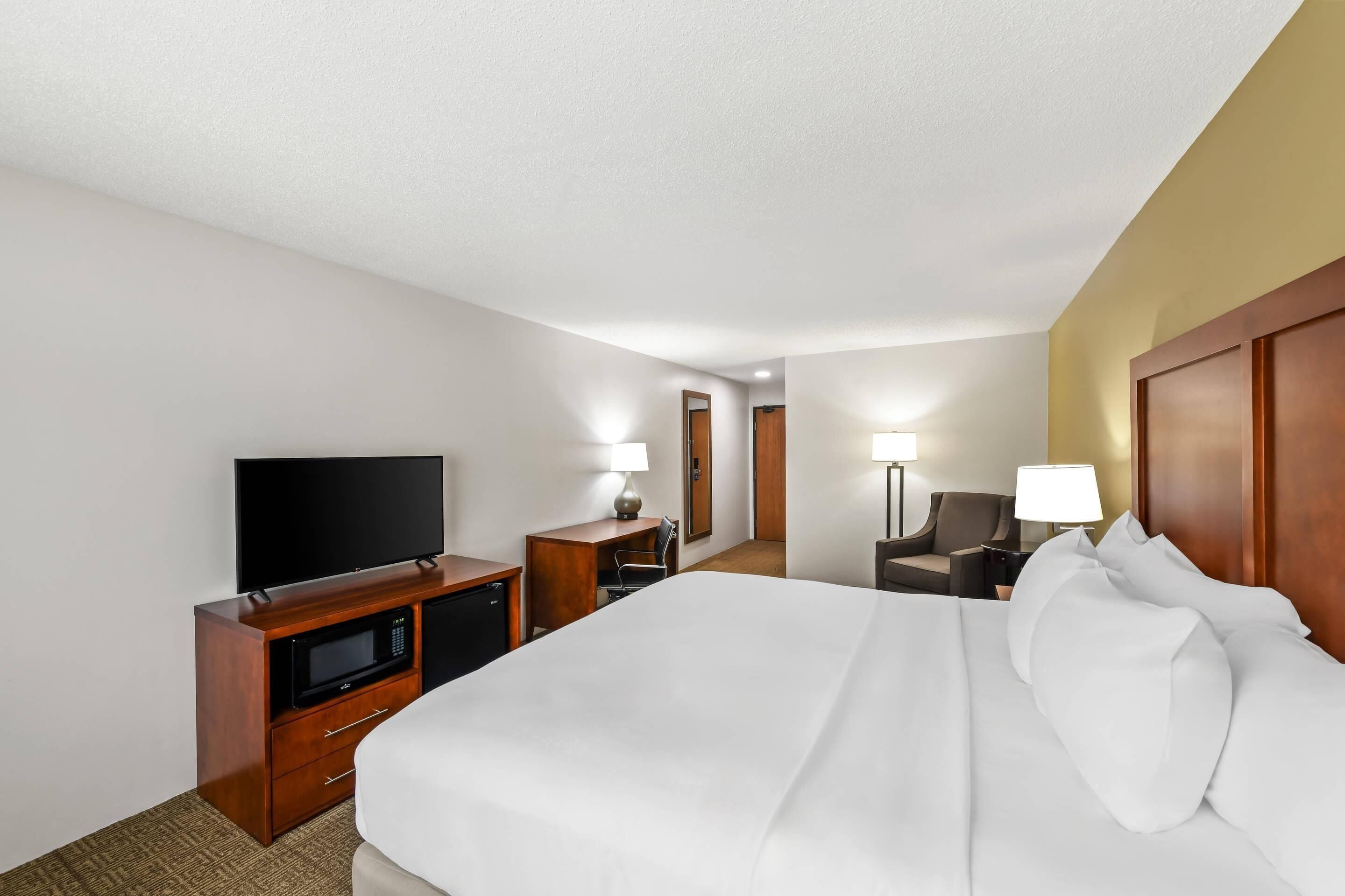 A hotel room with a large bed, a TV, a desk with a lamp, and a chair.