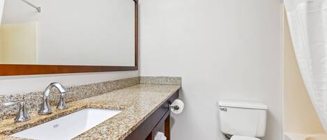 A bathroom with a granite countertop sink, a mirror, a toilet, and a shower curtain.