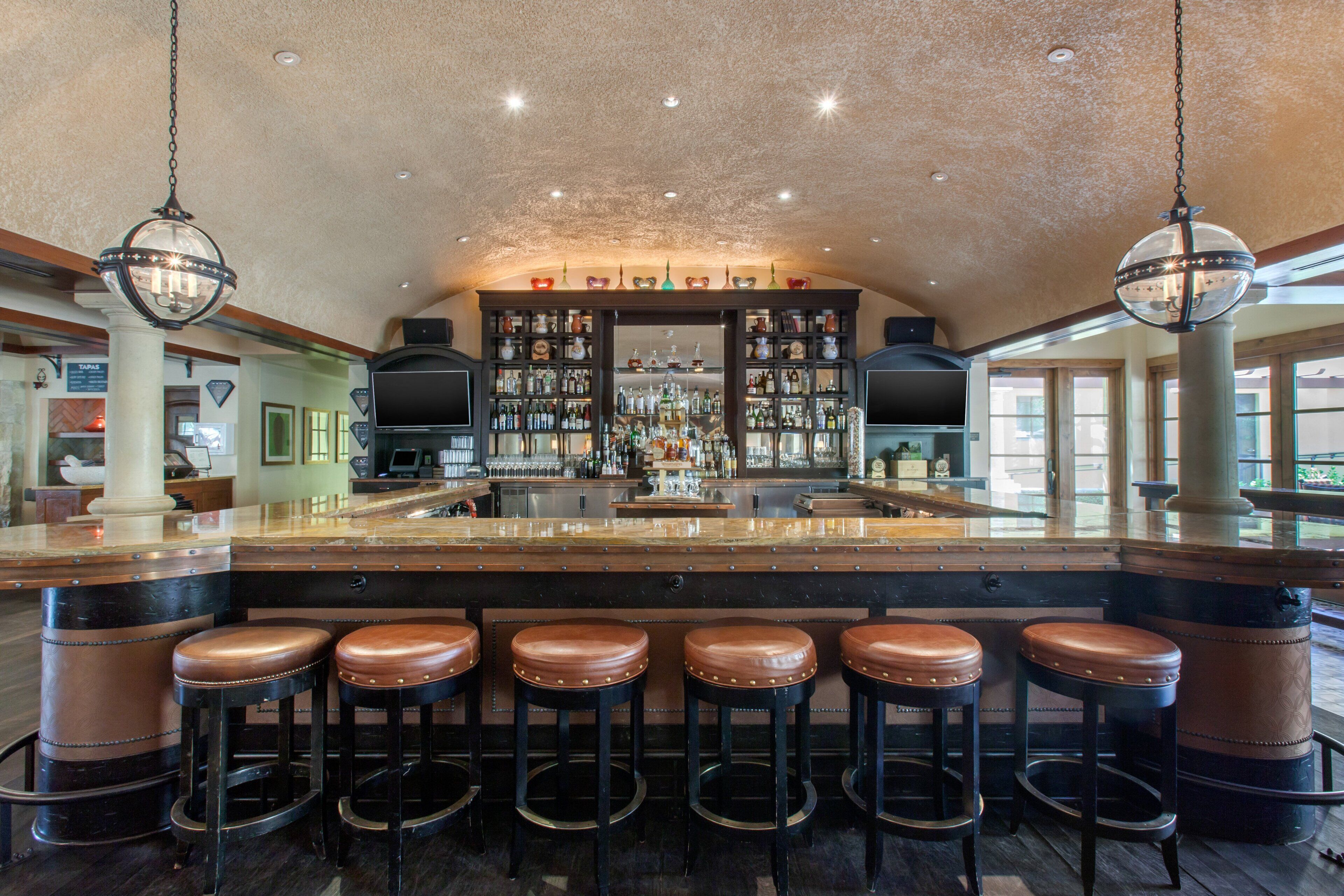 Un espace bar doté d’un grand îlot central, de nombreux tabourets et d’un bar bien garni.