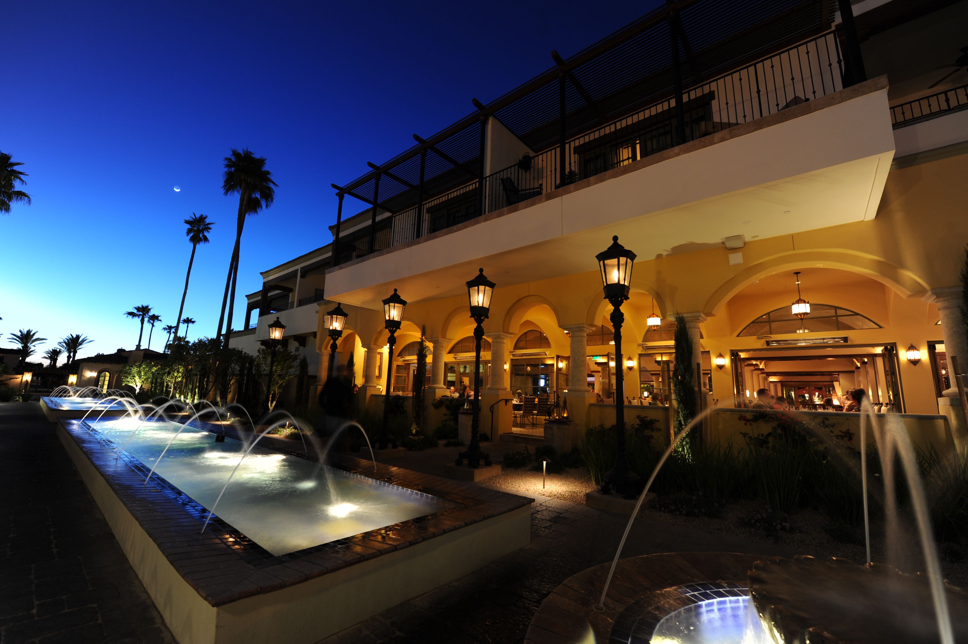 A hotel courtyard with a water feature, palm trees, and an arched entrance.