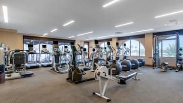 A gym with various cardio and strength training equipment, large windows, and a carpeted floor.