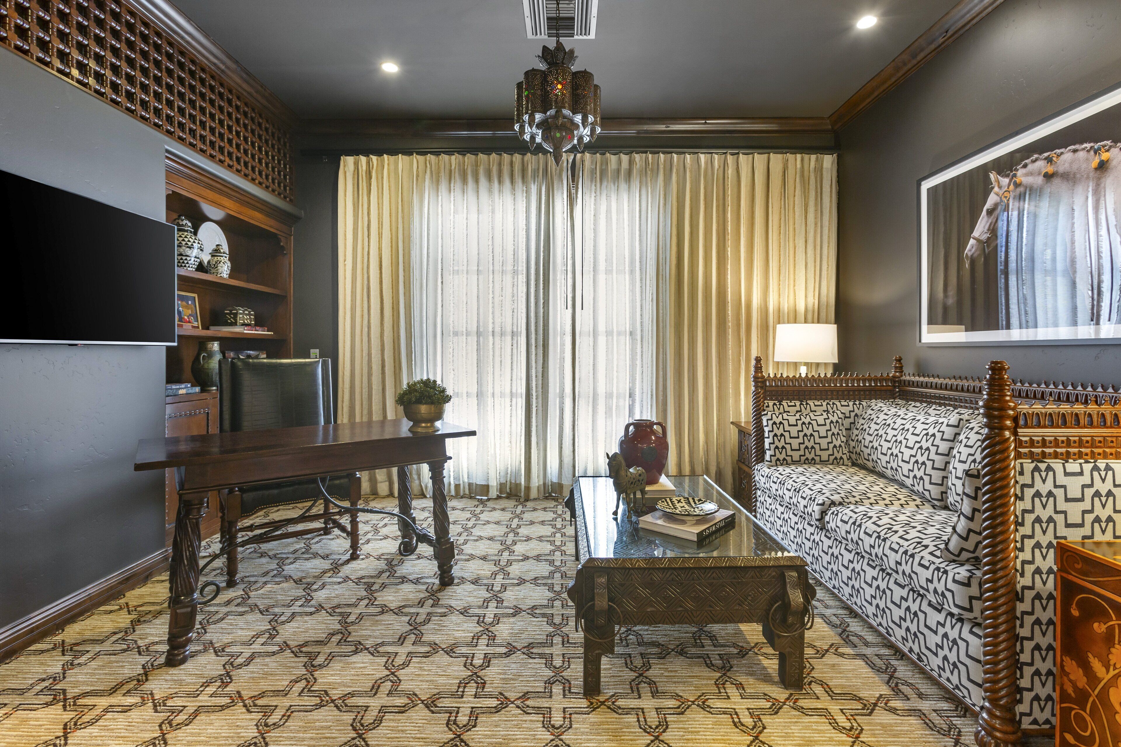 A living room with a patterned carpet, a wooden sofa, a coffee table, a television, and a chandelier.