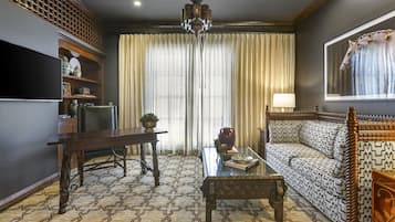 Una sala de estar con alfombra estampada, sofá de madera, una mesa de centro, televisor y candelabro.