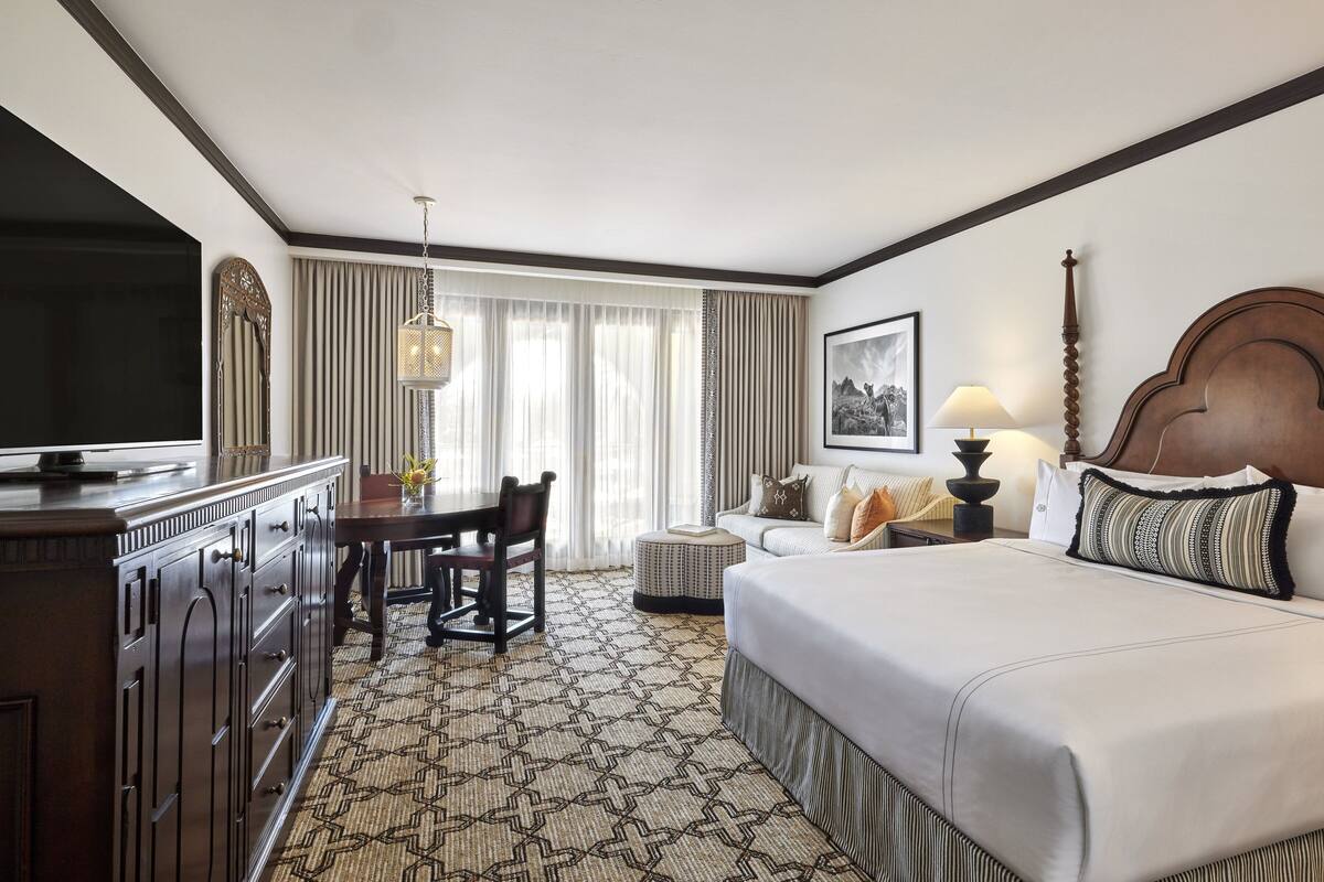 Een hotelkamer met een groot bed, een bureau met stoel, een televisie, een lamp en een lijst aan de muur.