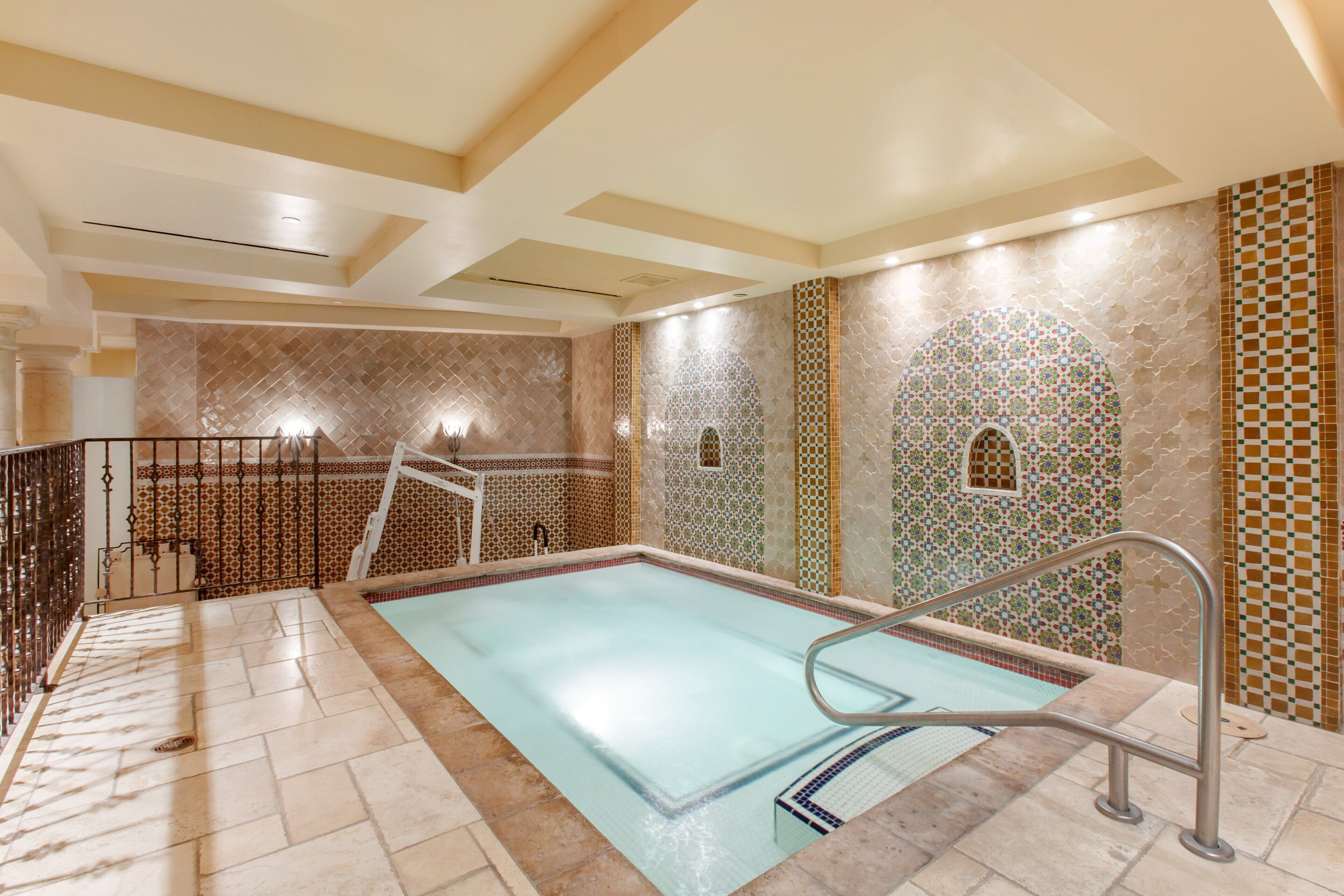 A swimming pool with a tiled deck, a metal railing, and decorative wall tiles.