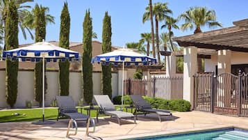 A pool area with lounge chairs and umbrellas, surrounded by palm trees and a fence.