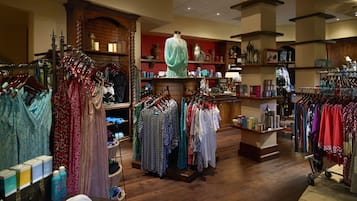 A clothing store with racks of dresses and shirts, wooden display shelves, and a mannequin.