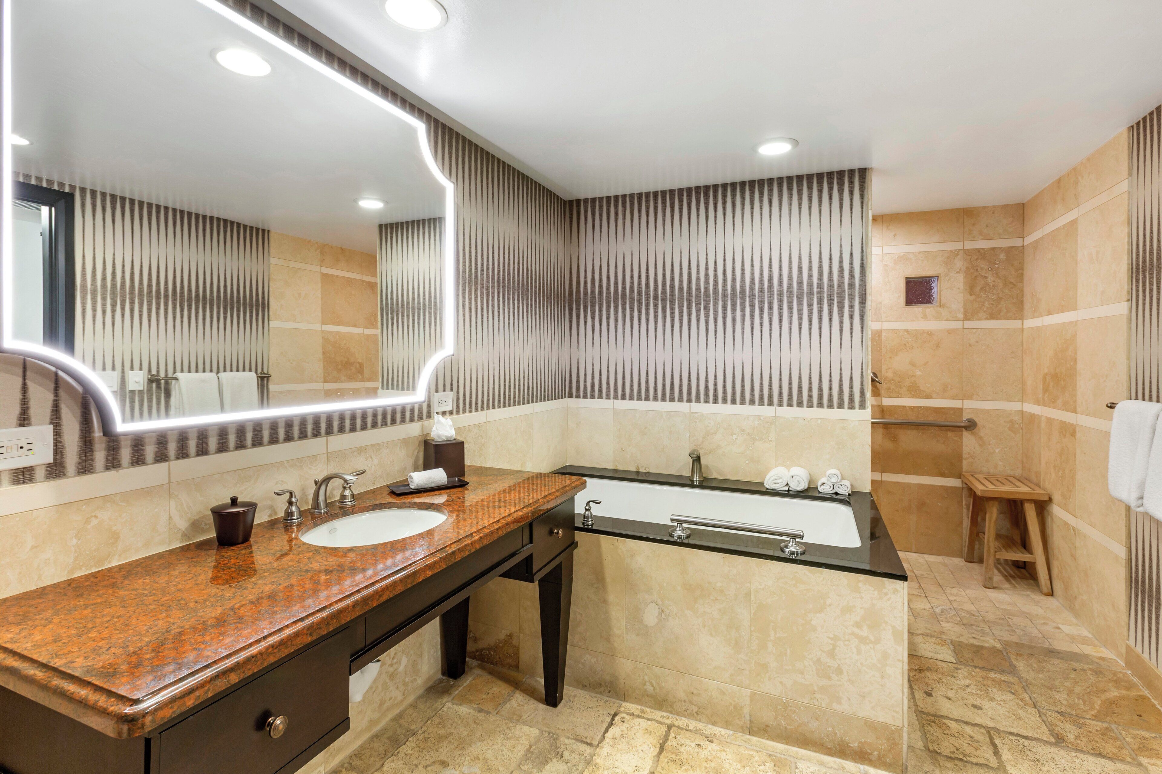 A modern bathroom with a granite countertop, a large mirror, a bathtub, and a shower area.