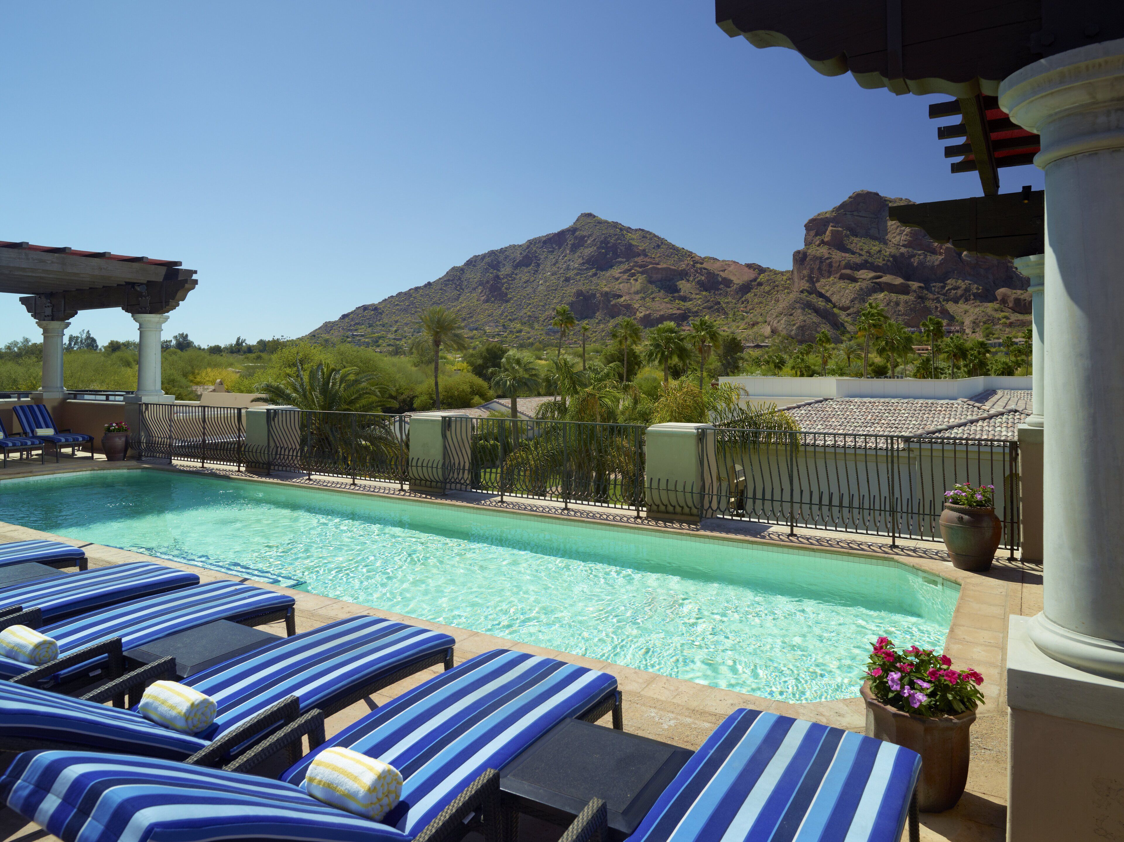 A pool area with lounge chairs, a pergola, and a mountain view.