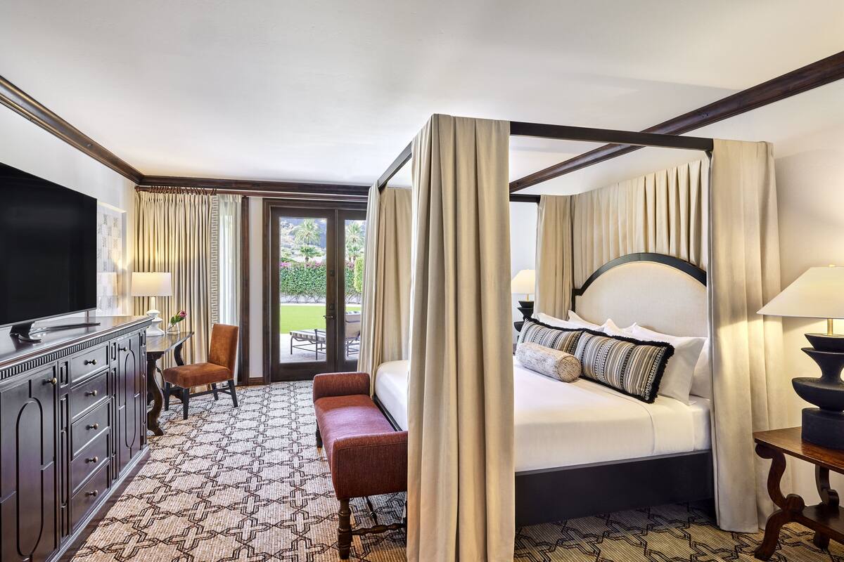Hotelkamer met hemelbed, televisie, bureau met lamp en uitzicht op het omliggende landschap.